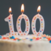 A 100th birthday cake with lit birthday candles that say100