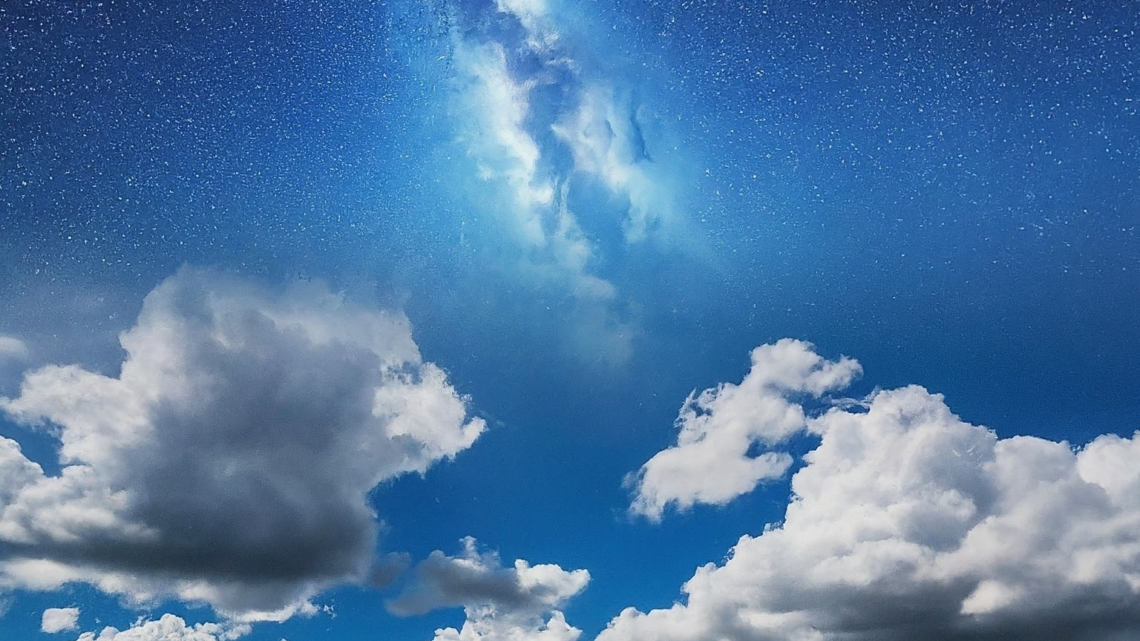 A creative image of a blue skyline with fluffy white clouds fading to an image of outer space above it.